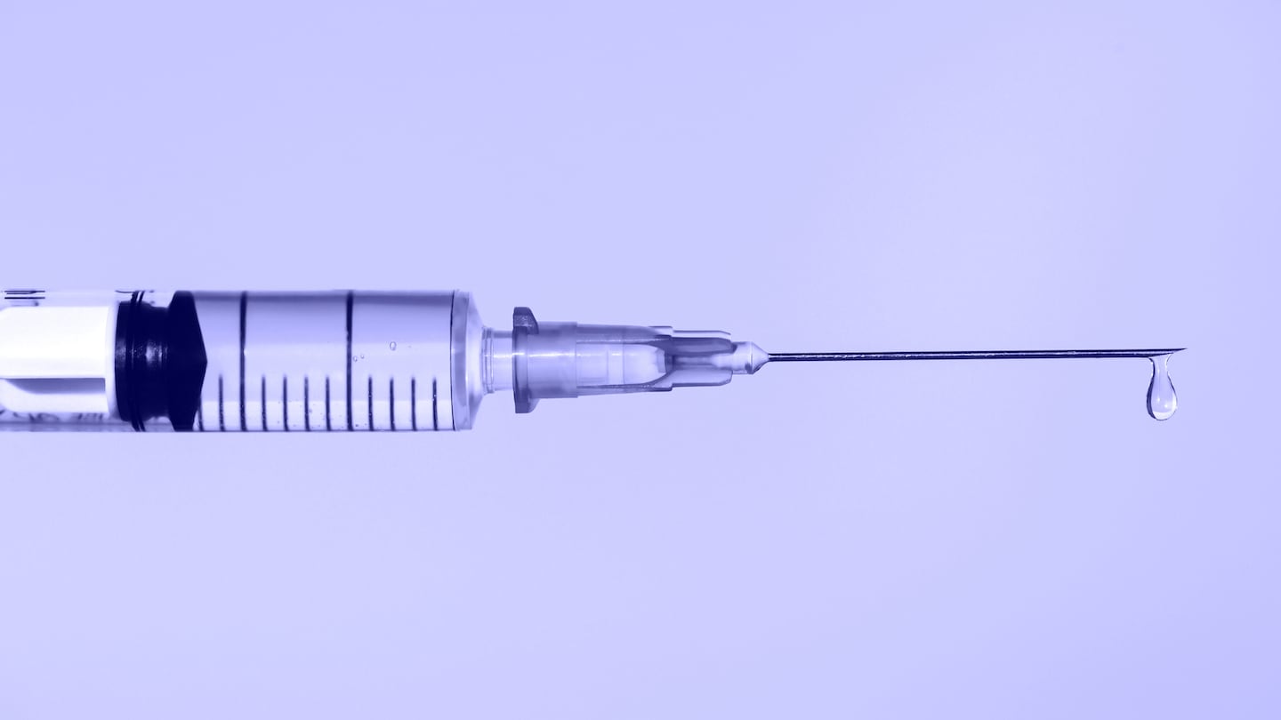 A disposable sterile syringe with drop of fluid medication on a thin needle on violet background.