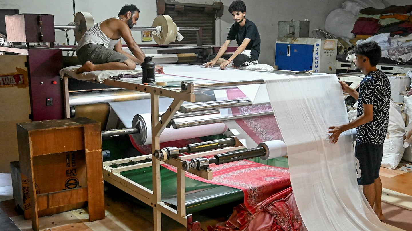 Workers check the design over a fabric by a printing machine at a garment factory in Amritsar, India on July 4, 2025.