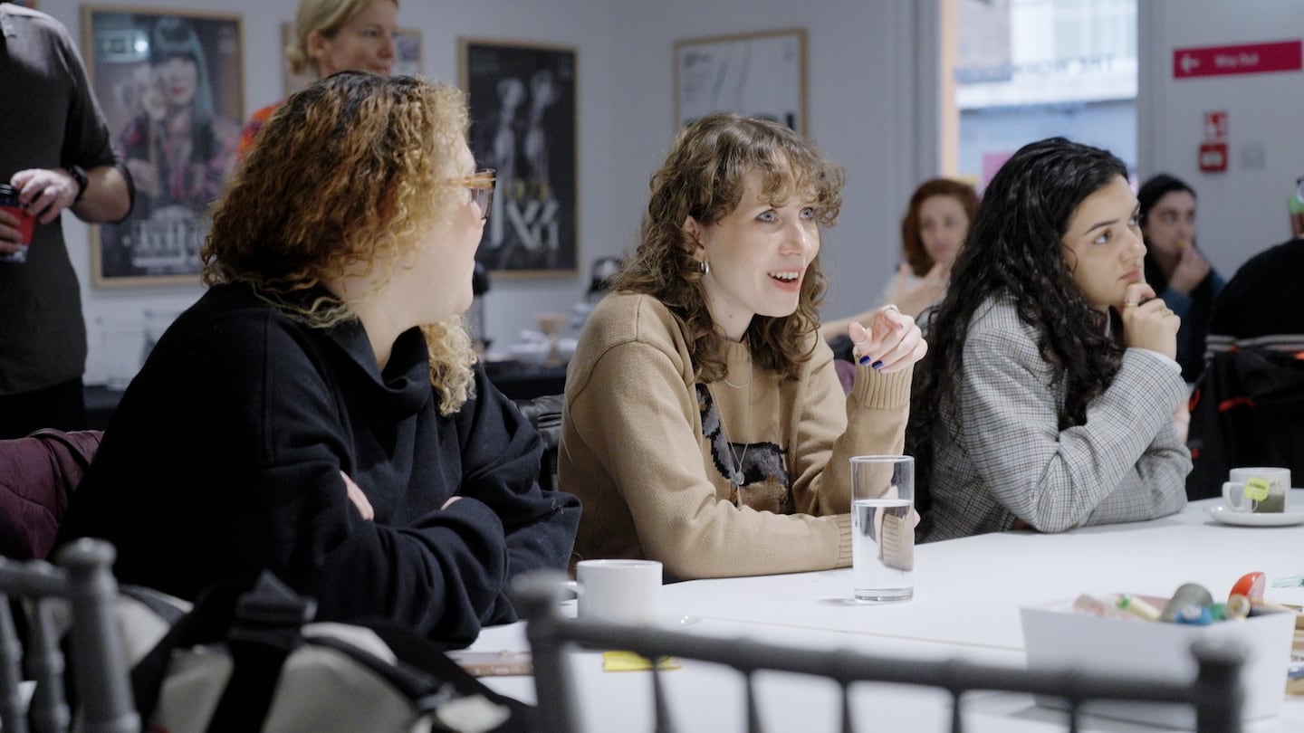 Students sit in a lecture room, engaged in conversation.